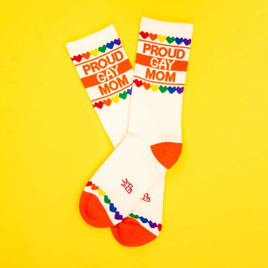Overlapping pair of white crew socks with orange heel/toe and colorful heart design, featuring “Proud Gay Mom” text