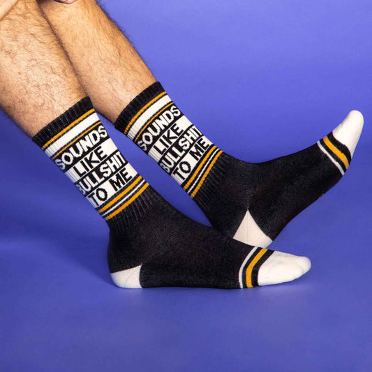 Black and white athletic-style socks with yellow stripes and the phrase “Sounds Like Bullshit To Me” worn by model
