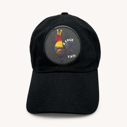 A black baseball cap featuring a circular embroidered patch on the front with a colorful rooster and the words 'COCK TAIL'.