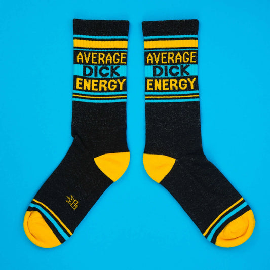 Black crew socks with yellow toe and heel, turquoise stripes, and bold text that reads Average Dick Energy. Flat lay on blue.