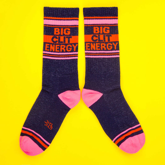 Pair of Navy and pink socks with orange accents on a bright yellow background, reading 'Big Clit Energy' in bold capital letters.