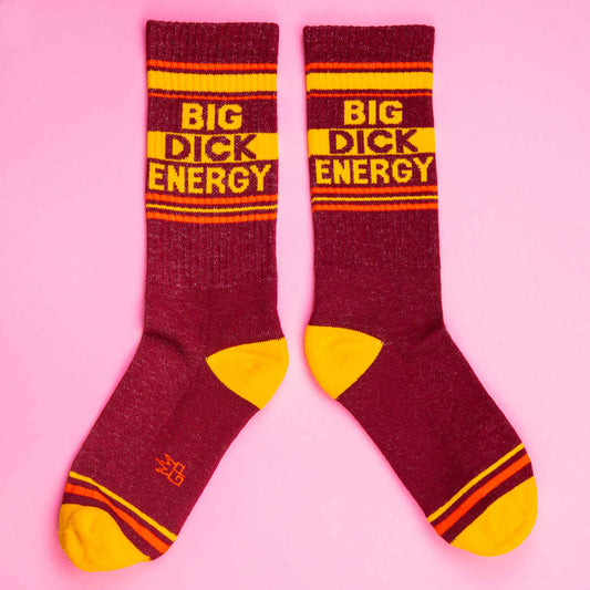 Pair of maroon and yellow socks on a pink background with the phrase 'Big Dick Energy' in bold yellow and maroon stripes.