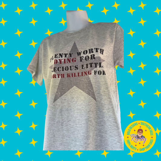 Gray T-shirt reading “Plenty Worth Dying For, Precious Little Worth Killing For” on turquoise background with yellow stars and Designed by Rusty logo in corner.