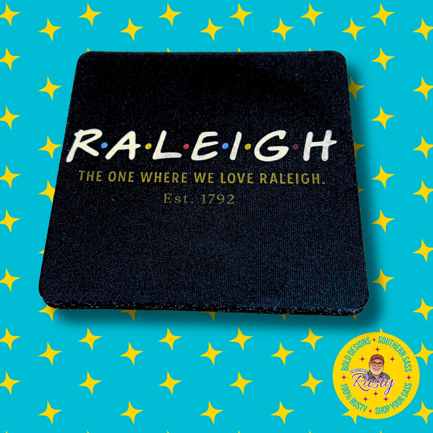 Raleigh Friends-themed coaster with bold white text and colorful dots, on turquoise DBR star background with Designed by Rusty logo.