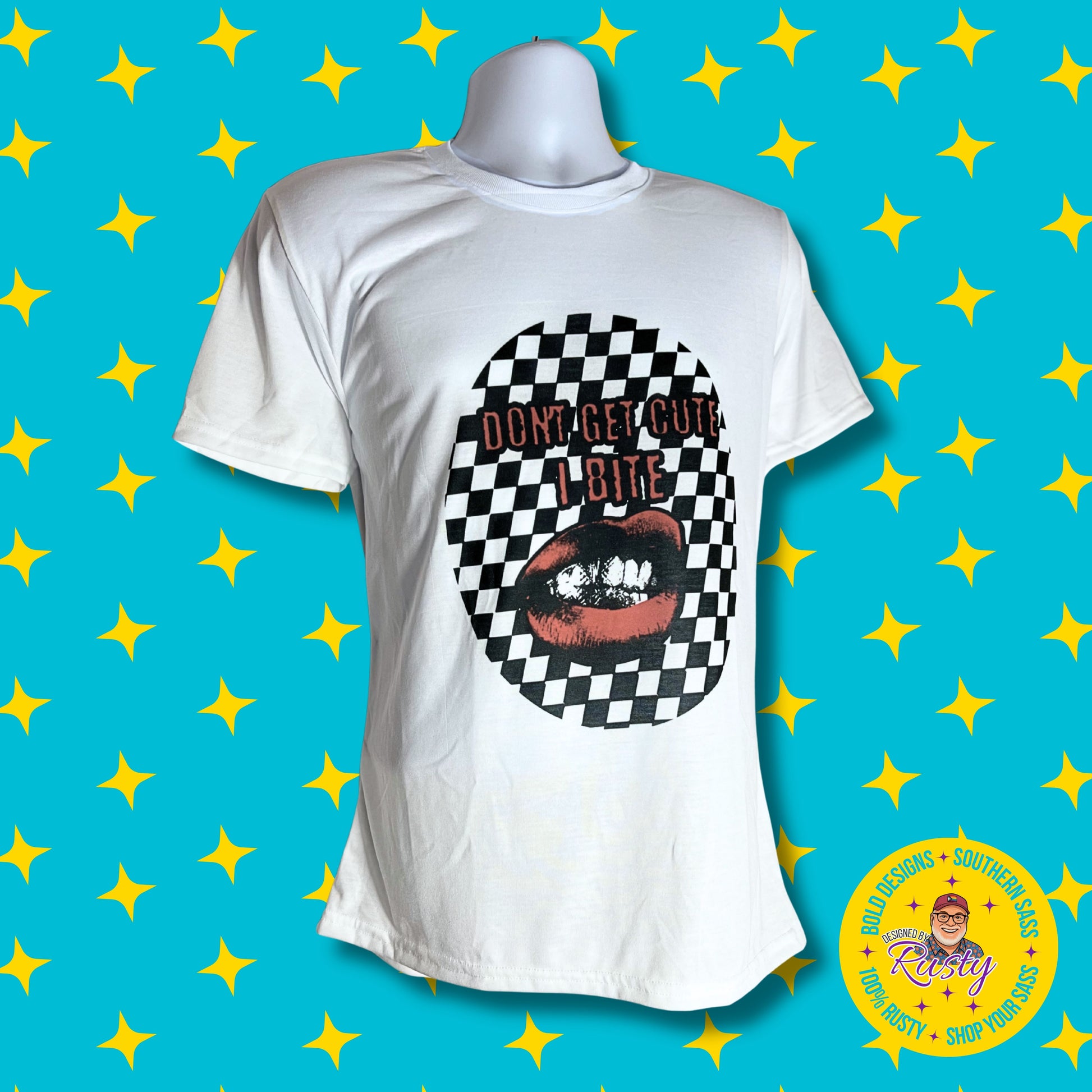 White T-shirt with “Don’t Get Cute, I Bite” design featuring red lips biting against a checkerboard pattern, displayed on mannequin with matching checkerboard backdrop.