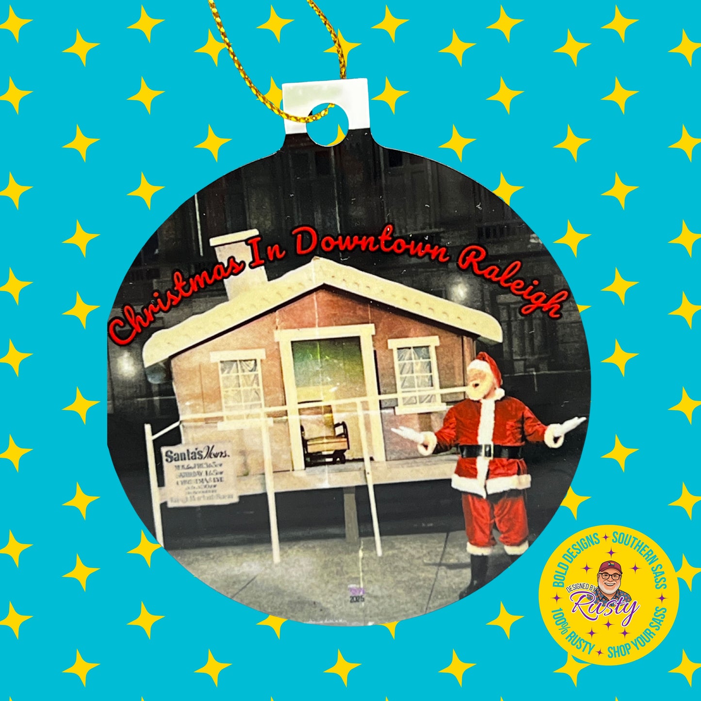Designed by Rusty Christmas ornament with downtown Raleigh Santa design on a turquoise background with yellow stars and DBR logo