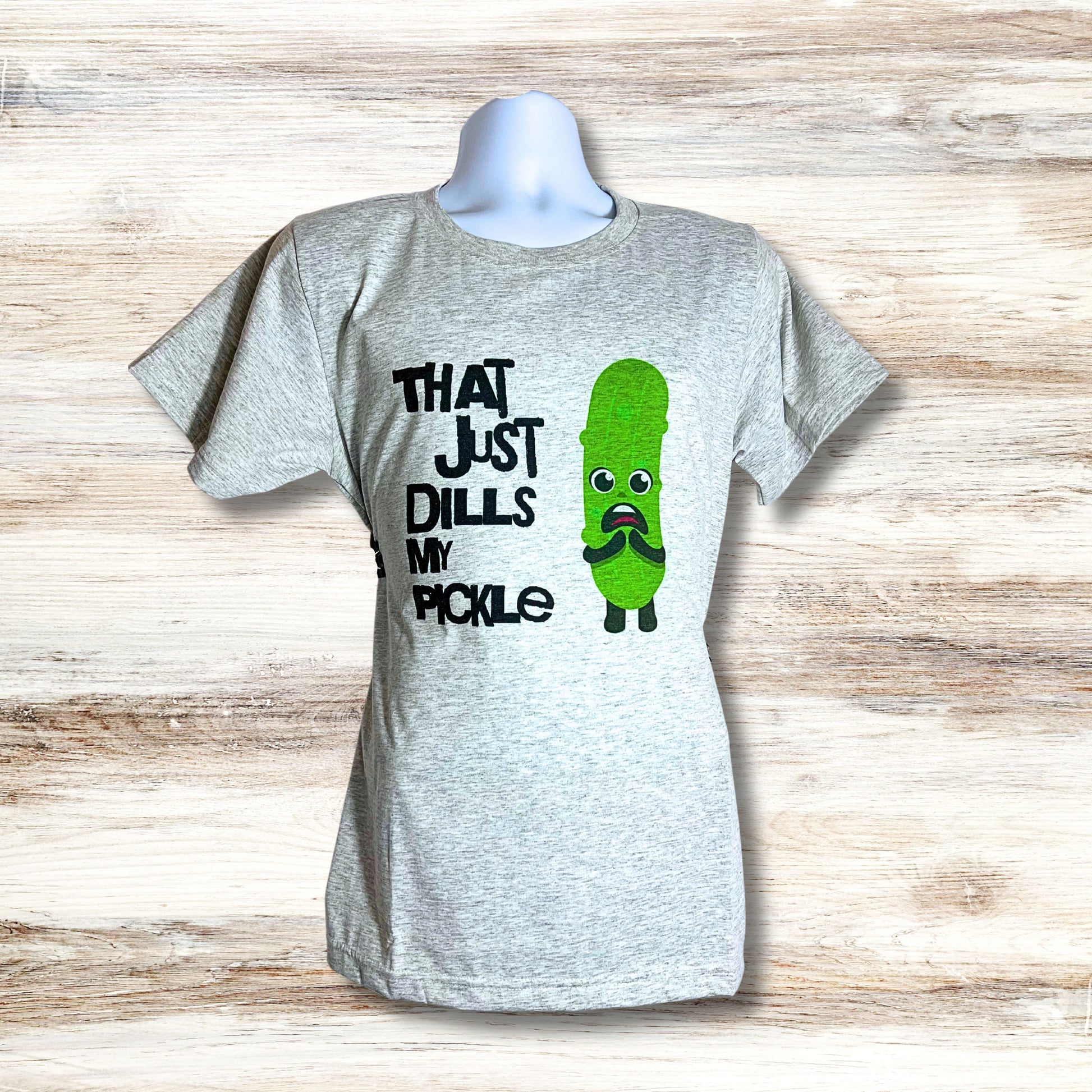 Light gray unisex t-shirt with “That Just Dills My Pickle” design, displayed against wood-textured backdrop.