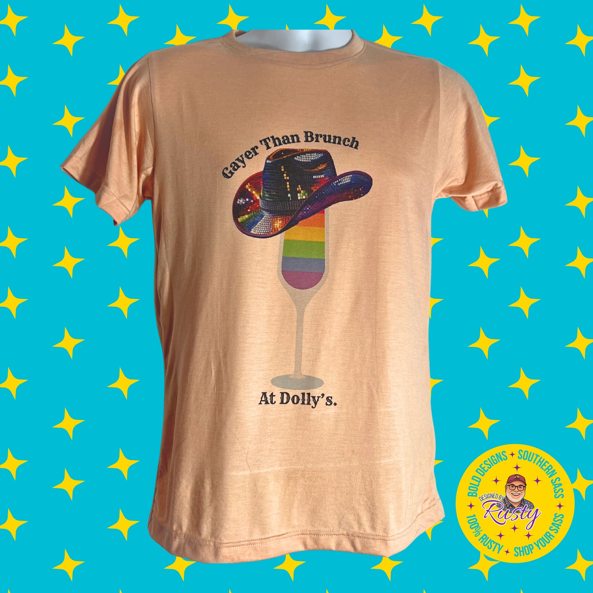 Peach T-shirt with “Gayer Than Brunch at Dolly’s” rainbow mimosa design and sequin cowboy hat, on turquoise background with yellow stars and Designed by Rusty logo.