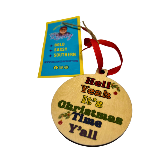 Round wooden Christmas ornament with colorful text reading ‘Hell Yeah It’s Christmas Time Y’all’ and a red ribbon.