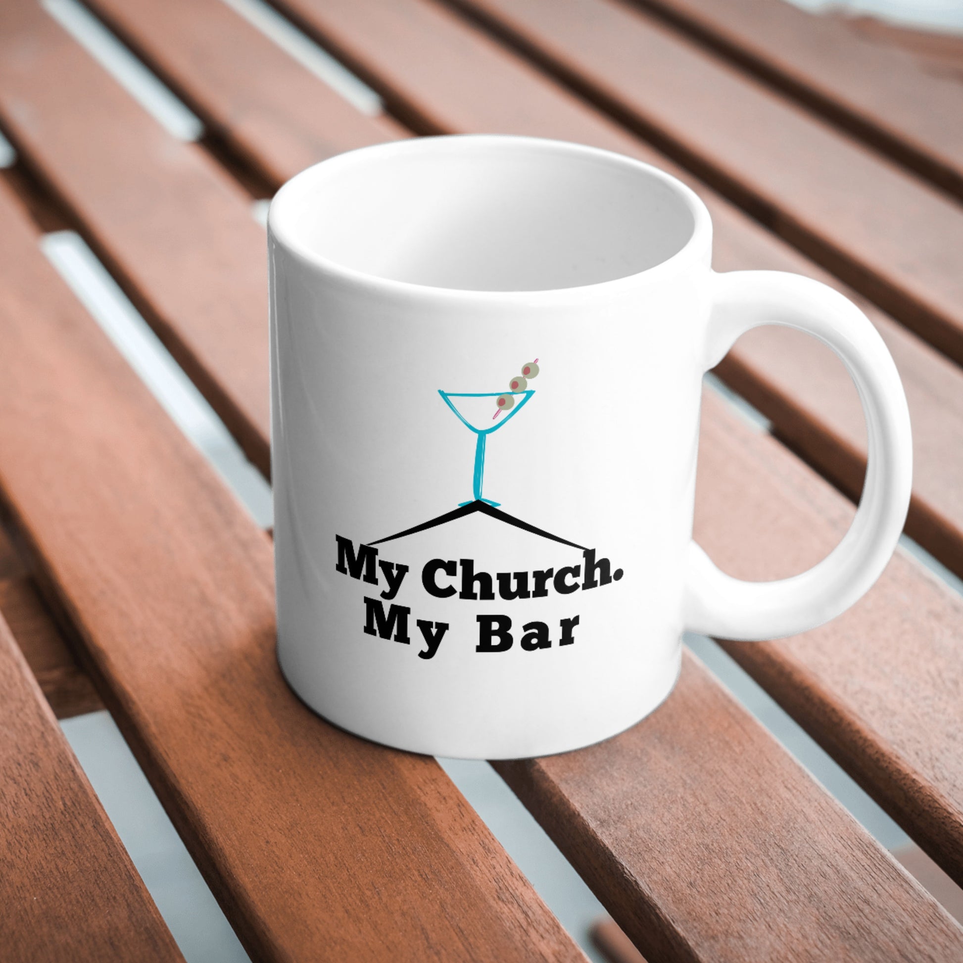 White ceramic mug with “My Church. My Bar.” text and martini glass design, displayed on a wooden tabletop with natural lighting.