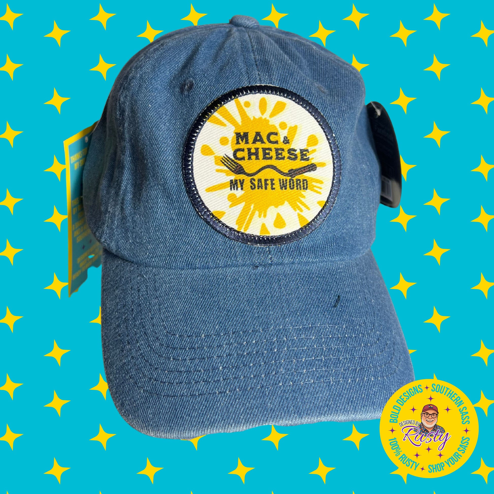 Denim embroidered patch hat with yellow splash design and bold text “Mac & Cheese My Safe Word,” on turquoise background with yellow stars and Designed by Rusty logo.