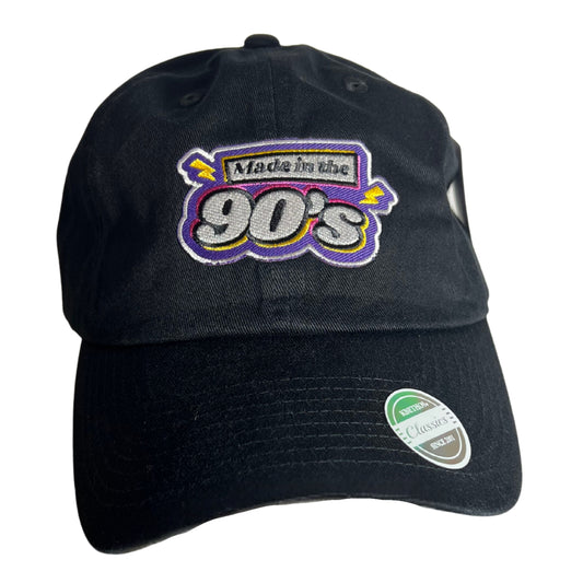 Black baseball cap with embroidered text “Made in the 90’s” in bold retro colors, displayed on a pure white background.