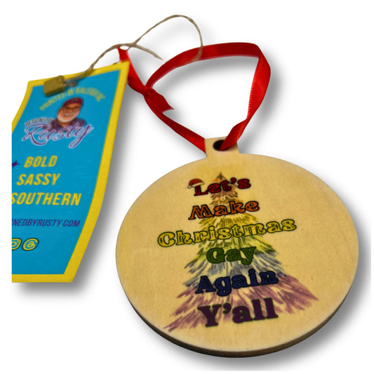 Round wooden Christmas ornament with rainbow text reading ‘Let’s Make Christmas Gay Again Y’all,’ tied with a red ribbon.