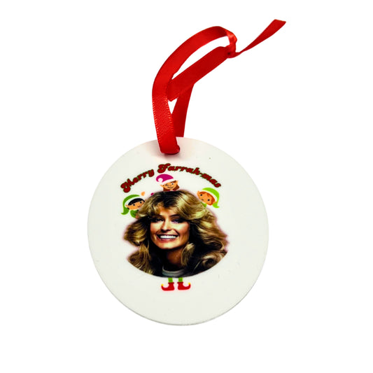 White aluminum Christmas ornament with a photo of Farrah Fawcett, surrounded by cartoon elves and the text “Merry Farrahmas,” hanging from a red ribbon.