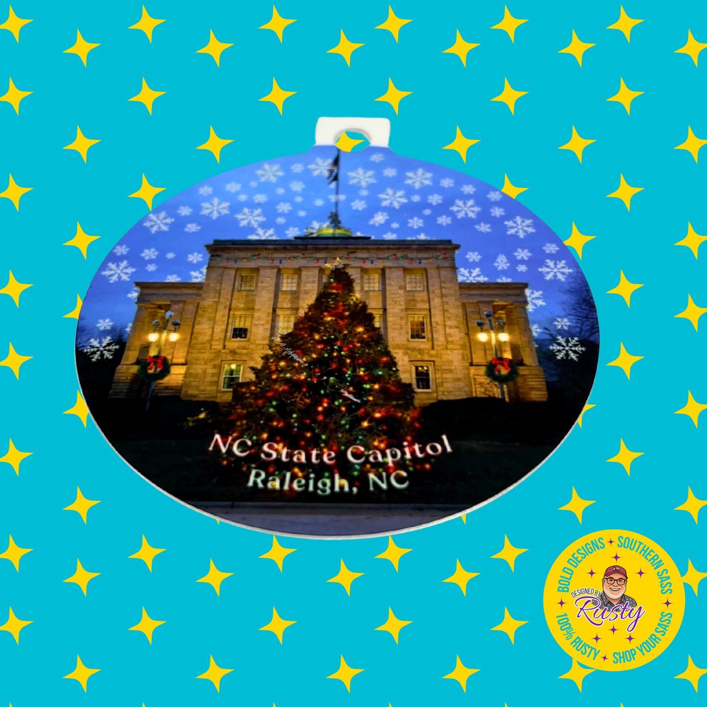 NC State Capitol Christmas ornament with snowflakes and holiday tree design, displayed on a turquoise background with Designed by Rusty branding.