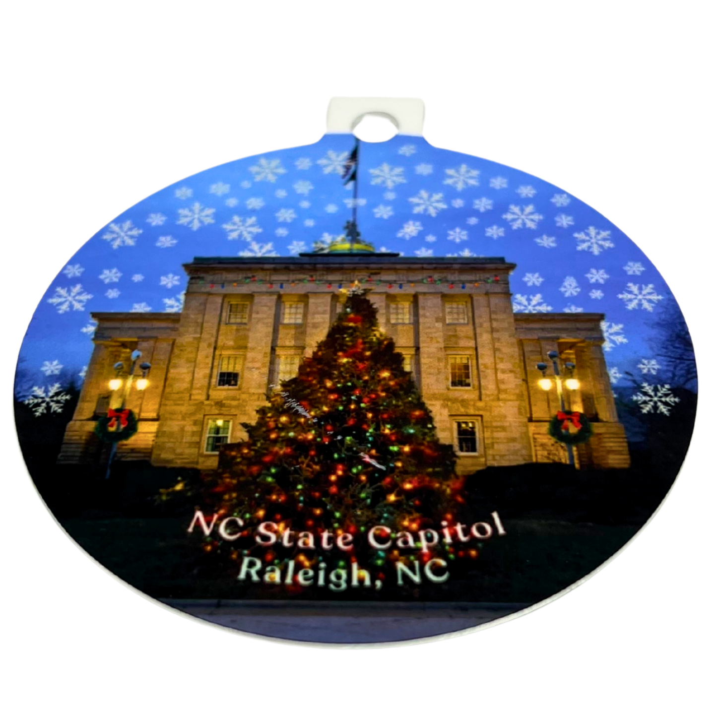 NC State Capitol Christmas ornament featuring the Raleigh State Capitol building with a lit Christmas tree and snowflake pattern on a round ceramic ornament.