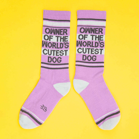 Cute dog owner pride socks with the phrase "Owner of the World's Cutest Dog" in black text, purple tones on a vibrant yellow background.
