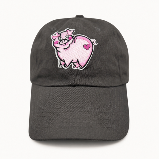 A dark gray baseball cap featuring an embroidered pink cartoon pig with a heart on the front, set against a plain white background.