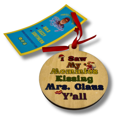 Round wooden Christmas ornament with colorful text reading ‘I Saw My Mommies Kissing Mrs. Claus Y’all,’ tied with a red ribbon.