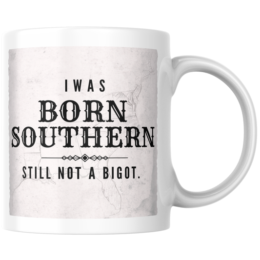 Primary: White ceramic mug with "Born Southern Still Not a Bigot" design on white background. Secondary: White ceramic mug with design on turquoise branded background with stars and DBR logo. Lifestyle: White ceramic mug held in hands in a cozy setting.