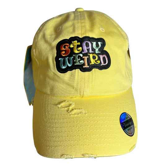Yellow embroidered patch hat with multicolor “Stay Weird” text, displayed on a pure white background.