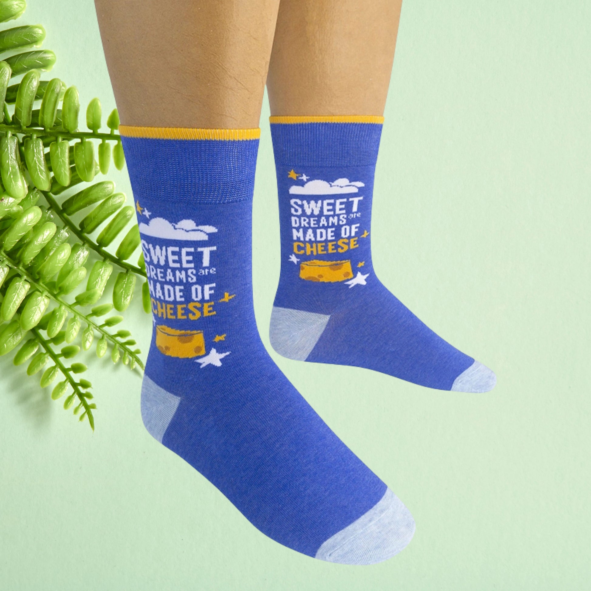 Blue crew socks with cheese graphic and text worn on feet against a soft green background.