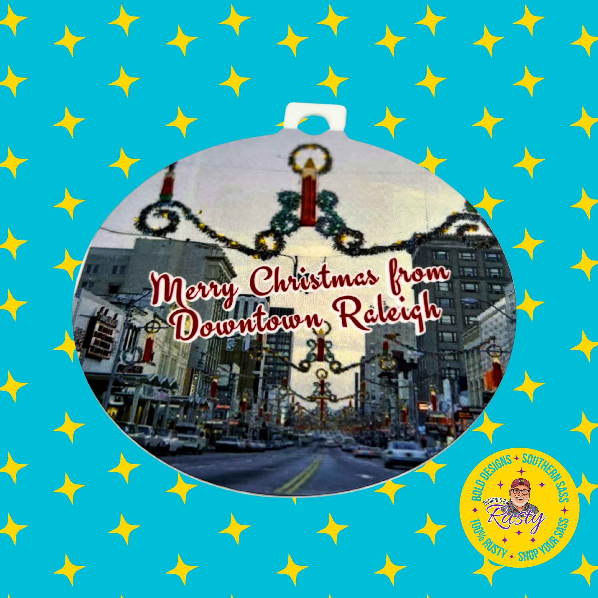 Vintage Downtown Raleigh Christmas ornament displayed on a turquoise background with yellow stars and Designed by Rusty branding.