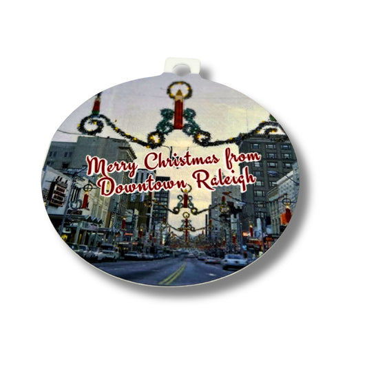 Round ceramic ornament featuring a vintage Downtown Raleigh street decorated for Christmas with the text ‘Merry Christmas from Downtown Raleigh,’ shown on a white background.
