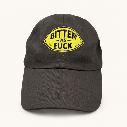 A dark gray cotton baseball cap featuring a yellow lemon-shaped embroidered patch on the front with the text 'BITTER AS FUCK' in black.