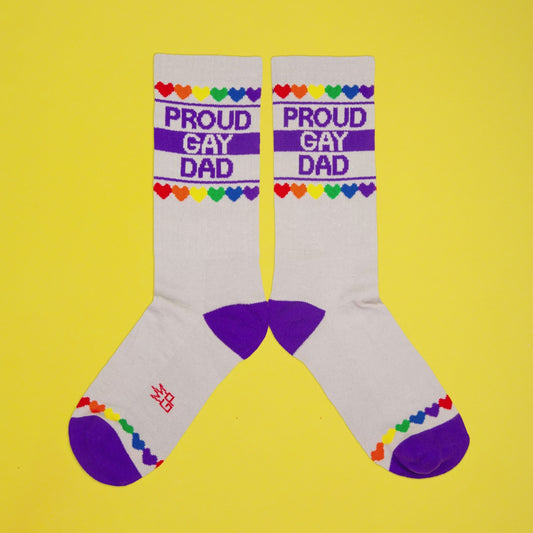 grayish crew socks with purple heel and toe, rainbow heart trim, and bold text: “Proud Gay Dad” on yellow background